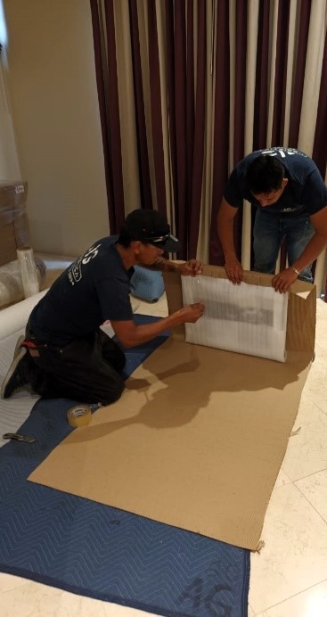 Two AG crew members carefully unpacking a framed art piece on a protective mat