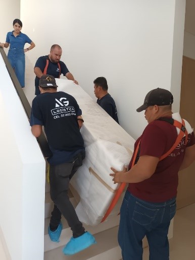 AG Logistics crew in branded uniforms carrying a wrapped piece up a residential stairway